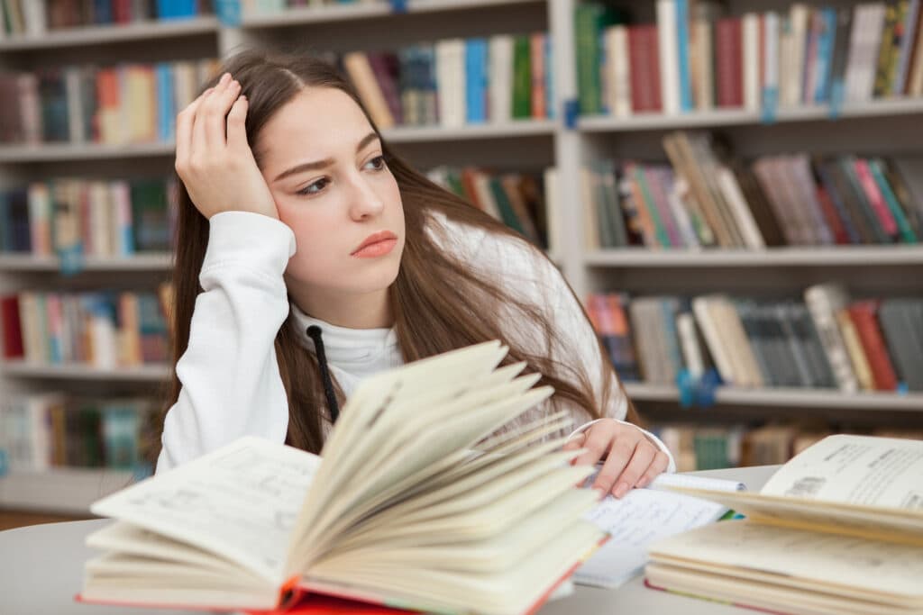 Studentin ist frustriert und abgelenkt in der Unibibliothek, weil sie mit dem Lernen überfordert ist.